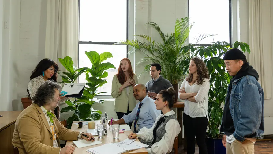 A team in discussion around a table in a bright room with large green plants